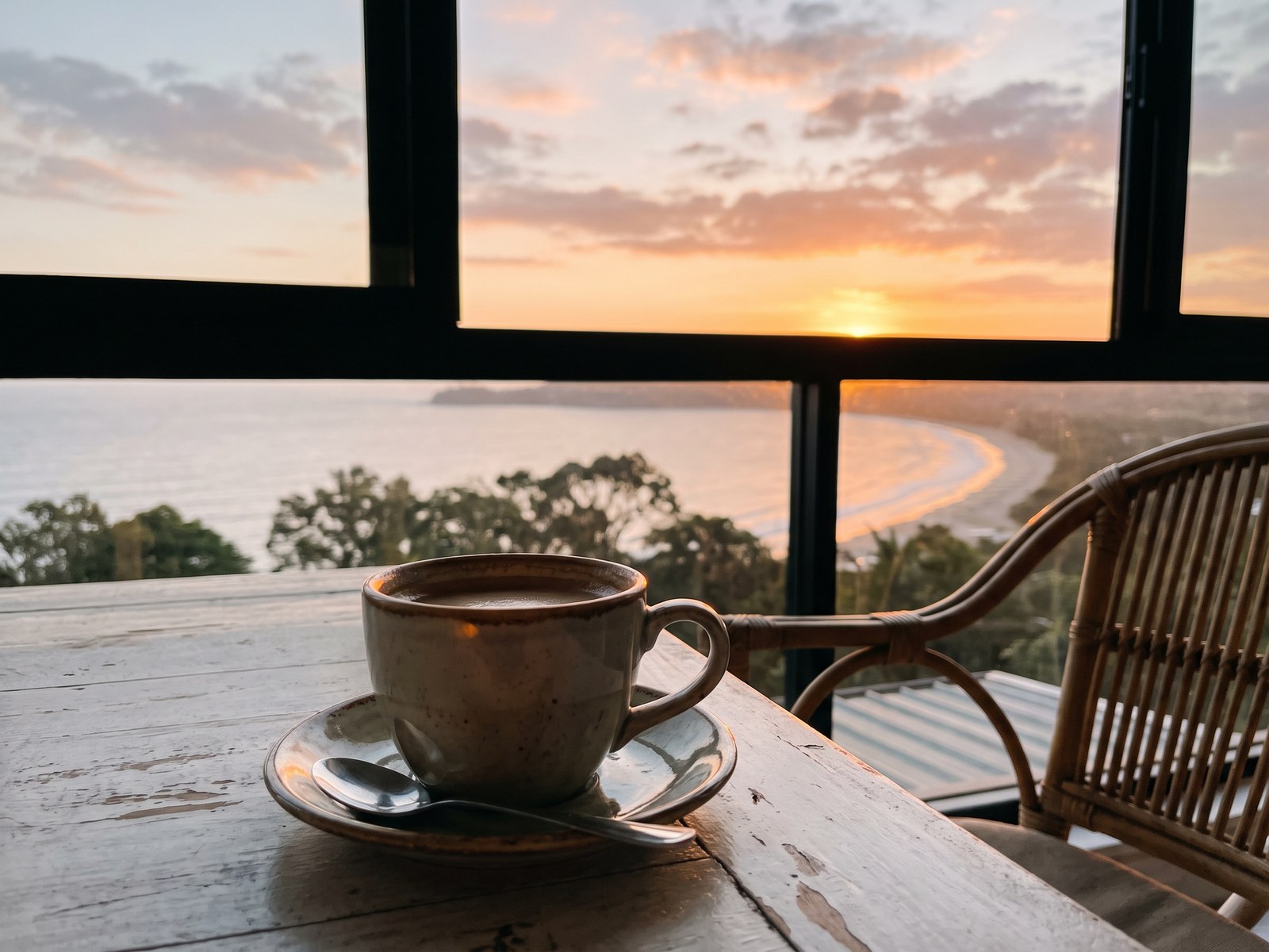 A cup of coffee on a balcony table at sunrise, looking out over a quiet bay