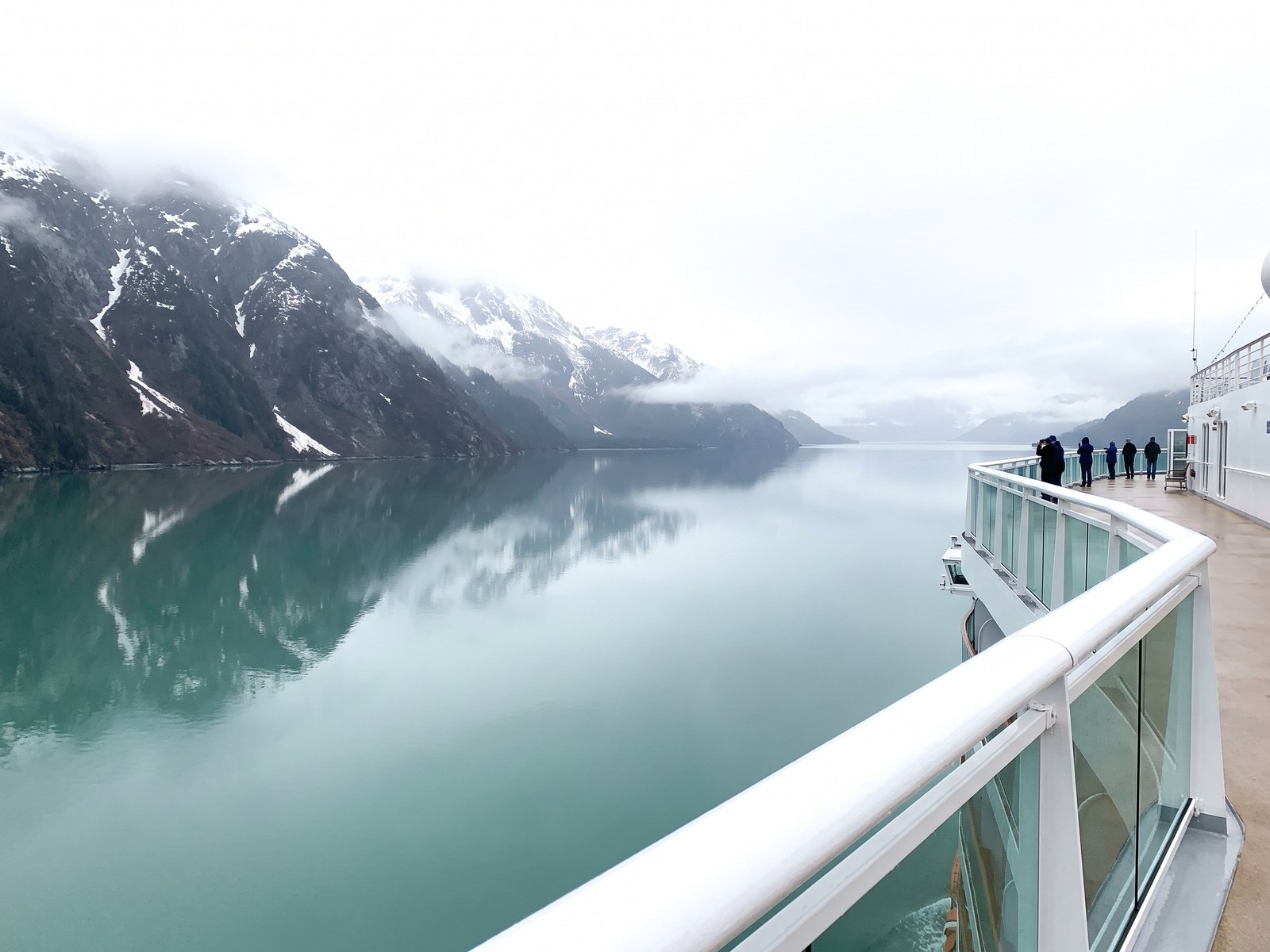 The view from a cruise ship railing across a still Alaskan fjord to snow-covered mountains